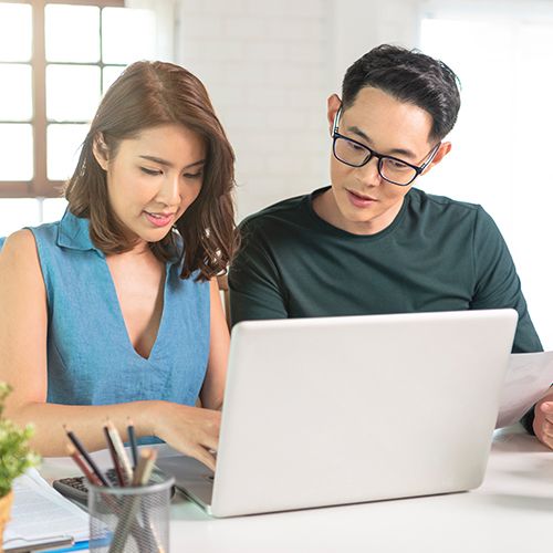 Two people working together at a table with a laptop and documents.