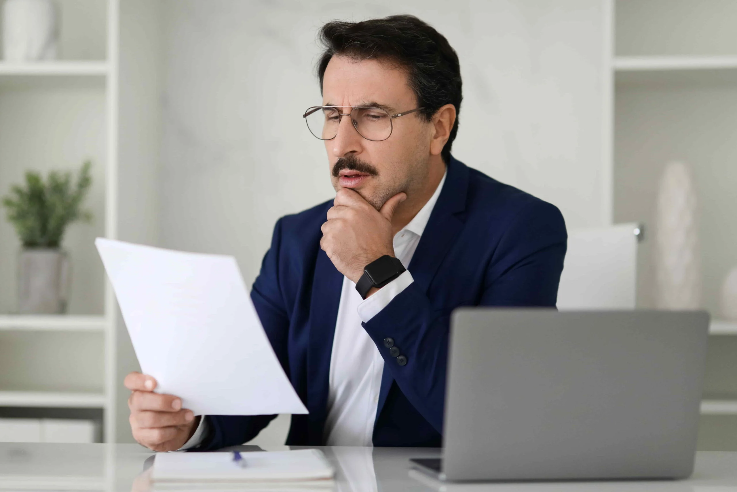 serious-businessman-blue-suit-critically-examining-document-while-sitting-his-desk